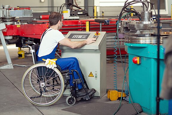 Mann im Rollstuhl bedient eine Maschine in einem Betrieb.